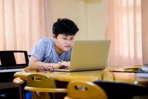 Selective focus to laptop computer and Asian cute boy using it to learning at Stock Photos