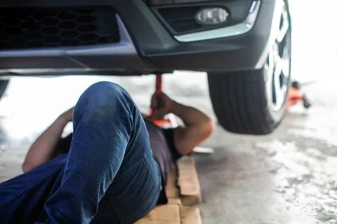 Selective focus to leg of mechanic lying on the ground under a lifted car p.. Stock Photos