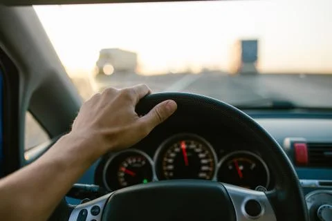 Selective focus man's hand on steering wheel, driving a car at sunset. Travel Stock Photos