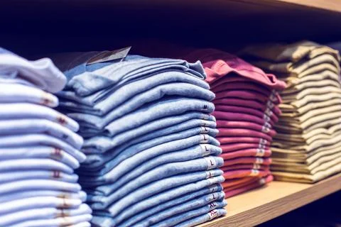 Selective focus to many clothes folded in the shop. Many stack of clothes. Stock Photos