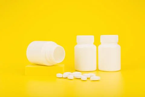 Selective focus, medication bottles and spilled pills on yellow background. The Stock Photos