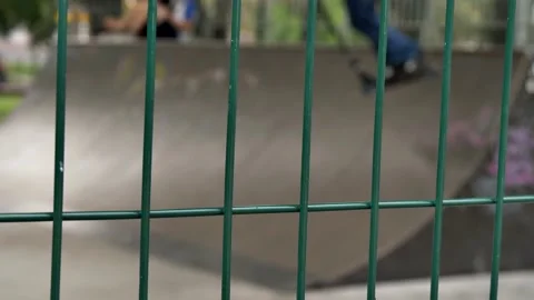 Selective focus on a mesh fence behind which children ride and do tricks in a sk Stock Footage 204092713