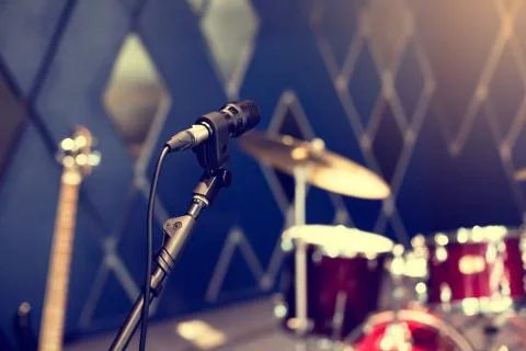 Selective focus to microphone with blurry rock band, drum set. Stock Photos