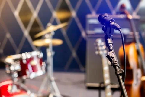 Selective focus to microphone with blurry rock band, drum set. Stock-Fotos