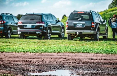 Selective focus on mud and torn up grass in the foreground of a dirt parking lot Foto stock