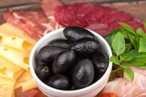 Selective focus on olives against the background of cuts of prosciutto, salam Stock Photos