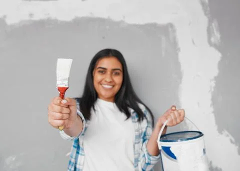 Selective focus on paintbrush while young woman holds up paint tin Stock Photos
