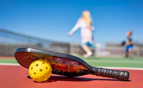 Selective focus on a pickleball and paddle on the court surface. Foto stock