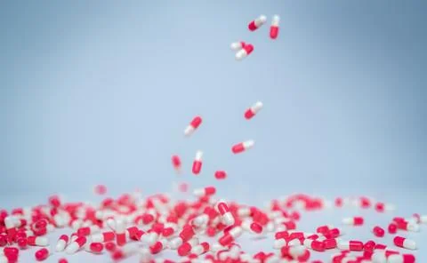 Selective focus on pink-white capsule pill fall down to white table. Antibiot Stock-Fotos