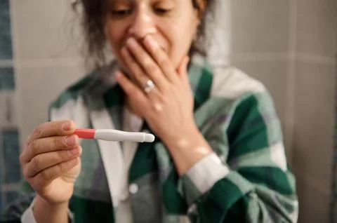 Selective focus on a pregnancy test in the hands of a blurred woman rejoicing at Stock Photos