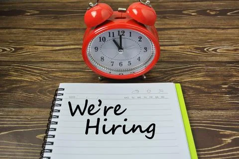 Selective focus of red watch, notebook written with WE ARE HIRING. Job opport Stock Photos