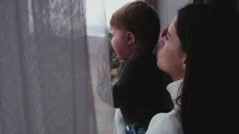 Selective focus of sad baby crying sitting on windowsill in arms of caring mom Stock Footage 166609671