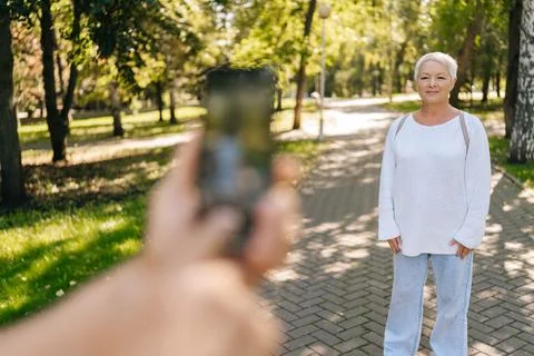 Selective focus shot of gray-haired senior woman posing happily in sunny park Stock Photos