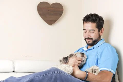 A selective focus shot of a Hispanic man hugging a cavapoo puppy sitting on a Fotos de archivo