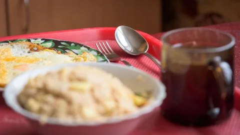 Selective focus on spoon, fork. Blurred oatmeal, scrambled eggs, cup of tea. Stock Photos