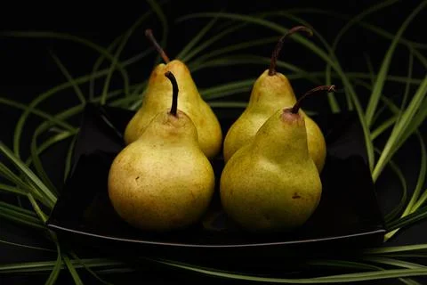 Selective focus, still life in dark tones with pears on black plate decorated Stock Photos