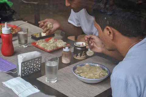 Selective focus of two young guys eating tibetan food at indoor cafe  Stock Photos