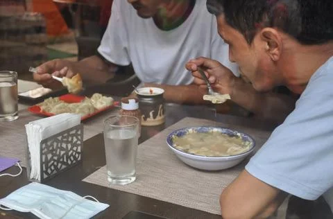 Selective focus of two young guys eating tibetan food at indoor cafe  Stock Photos