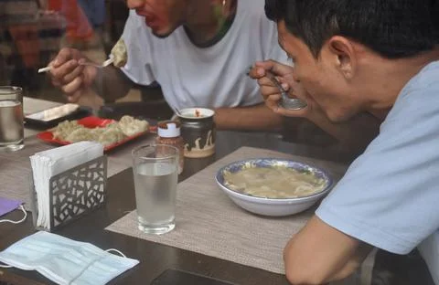 Selective focus of two young guys eating tibetan food at indoor cafe  Stock Photos