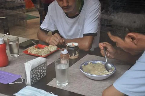 Selective focus of two young guys eating tibetan food at indoor cafe  Foto stock