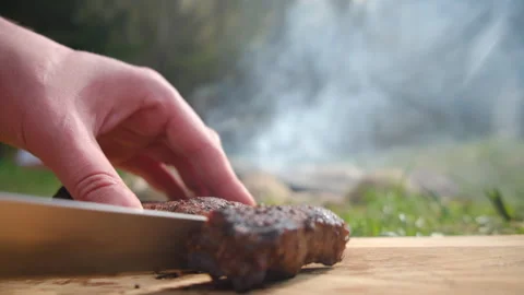 Selective focus of unknown man cutting hot beef steak just cooked on bonfire Stock Footage 271629153