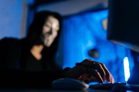 Selective focus of unrecognizable hooded hacker man wearing anonymous mask using Stock Photos