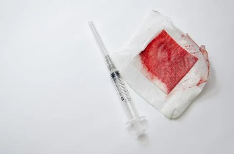 Selective focus white plaster with blood and syringe isolated on white. Stock Photos
