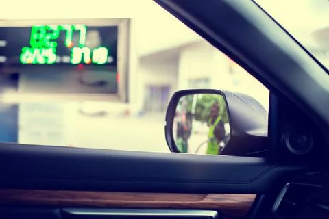 Selective focus to wing mirror with blurry fuel price display board and the o Stockfoto's