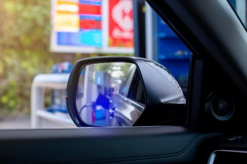 Selective focus to wing mirror with blurry fuel price display board. Stock Photos