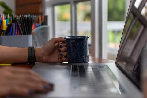 Selective focus on a woman's hands with a cup of coffee, sitting in home office Stock Photos