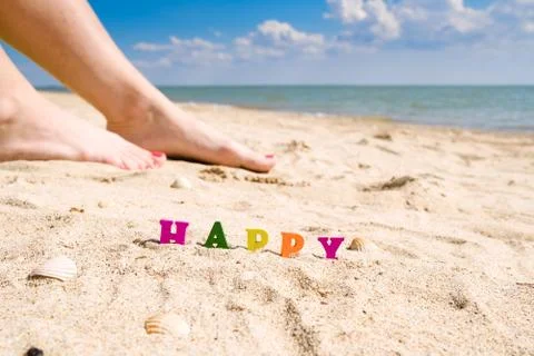 Selective focus on the word Happy on the background of female feet and the sea. Stock Photos