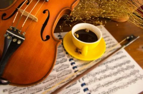 In selective focus of the yellow ceramic coffee cup put beside classic violin 스톡 사진