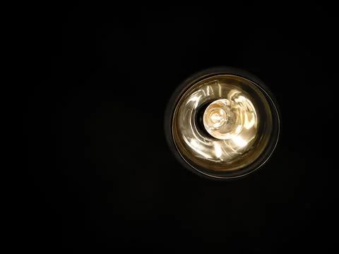Selective focus yellow light bulb in round chandelier on black background. Stock Photos