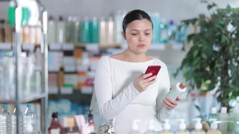 Selective middle-aged woman scanning QR-code on shampoo or gel bottle in Stock Footage 313874689