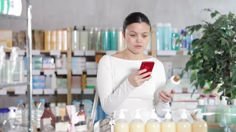 Selective middle-aged woman scanning QR-code on shampoo or gel bottle in Stock Footage 325028860