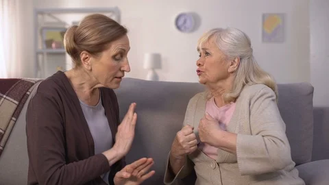 Self-assertive old women arguing and offending each other sitting in living room