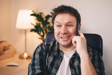 Self-employed young man talking on his mobile phone, smiling while sitting in Stock Photos