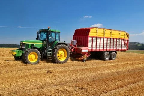 Self loading wagon attached to green tractor, picking up and transporting of str Stock Photos