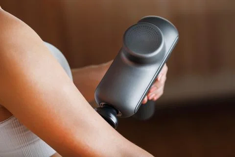 Self-massage of women's hands using a percussion gun at home. Stock Photos