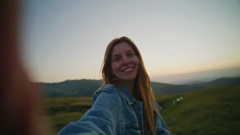 Self-portrait taken during sunset in a grassy area with hills in the background Stock Footage 345683822