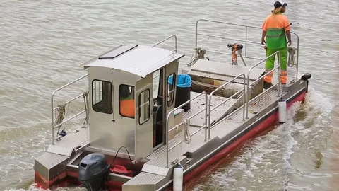 Self-propelled barge going down river, carrying workers and trash bin onboard Stock Footage
