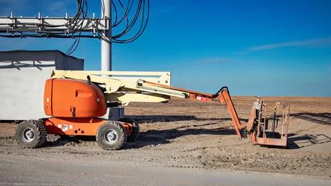 A self-propelled telescopic tower is parked on a dirt path near a construct.. Stock Photos