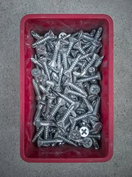 Self-tapping screws in a red plastic box, close-up top view, flat frame. Stock Photos
