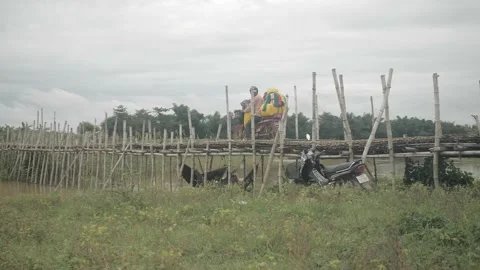  Seller carrying stack of clothes while crossing a bamboo bridge  Stock Footage 167399378
