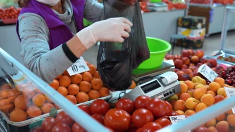 The Seller with facemask putting tomatoes on the counter for sale. Coronavirus Stock Footage 132881182