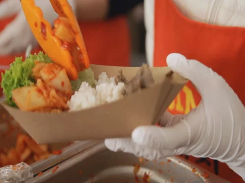 Seller is putting japanese food into a cardboard plate at the street food Stock Footage