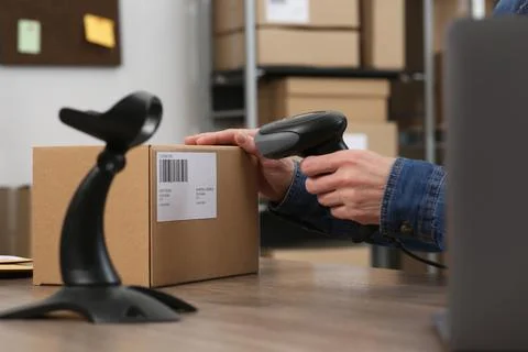 Seller with scanner reading parcel barcode at table in office, closeup. Onl.. Photos