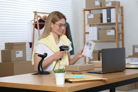 Seller with scanner reading parcel barcode in office. Online store 스톡 사진