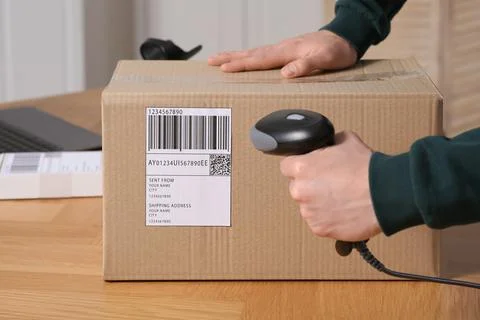 Seller with scanner reading parcel barcode at table in office, closeup. Onl.. Foto stock