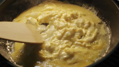 A semi-cooked scramble eggs are stirred with a wooden spatula 스톡 동영상 152649655